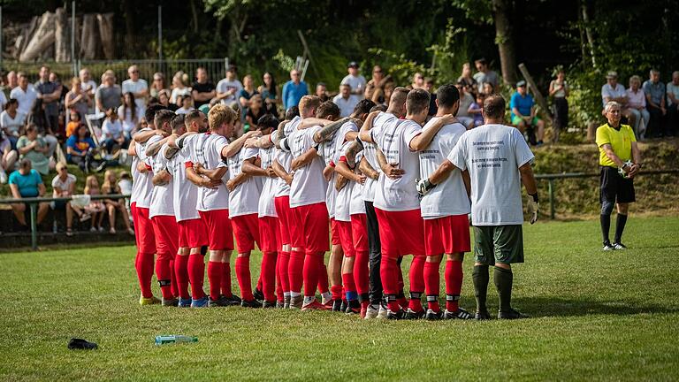 Gedenkminute beim Benefizspiel des TSV Sackenbach gegen den TSV Partenstein. Zuschauer und Mannschaft trugen ein Spenden-Shirt mit der Aufschrift 'Du bist für immer in unseren Herzen, wir sind eine Familie'.