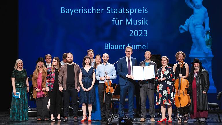 Bayerischer Staatspreis für das Würzburger Projekt 'Der Blaue Eumel'. Bei der Verleihung im Münchner Cuvilliéstheater von links: Laudatorin Evelyn Meining, Eumelnauten und - mit Urkunde - Kunstminister Markus Blume sowie Vereinsvorsitzender Tobias Schirmer.