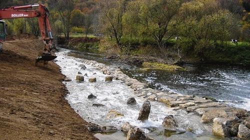 Fischtreppe am Tauberwehr ist fertig       -  Distelhausen (ubü) Nach rund 14-tägiger Arbeit sind nun die Bauarbeiten am Umgehungsgerinne beim Tauberwehr in Distelhausen abgeschlossen. Bauträger war die Tauberfischereigenossenschaft, die Bauaufsicht und Planung hatte Egon Gebauer inne. Das Grundstück wurde kostenlos von der Distelhäuser Brauerei zur Verfügung gestellt. Mit der Maßnahme soll Fischen und Kleinlebewesen der Aufstieg zum Oberwasser ermöglicht werden. Zuvor musste die Böschung aufgebaut werden. Zum  Schutz einer Quelle wurden Abdichtungsbahnen verlegt, die dann  mit Beton, Steinen und Erde abgedeckt wurden. Im Anschluss wurde die Böschung mit Erde und Humus aufgefüllt. Der Steigwall wurde in einer Breite von 3,50 Meter und einer Länge von 130 Metern angelegt. Um Kanufahrer an der Einfahrt zu hindern, wurden dort hohe Steine aufgestellt. Mitarbeiter des Betriebshofs Tauberbischofsheim bepflanzten die Böschung neu bepflanzt. Seit Dienstagmittag läuft nun das Wasser durch das neue Umgehungsgerinne.