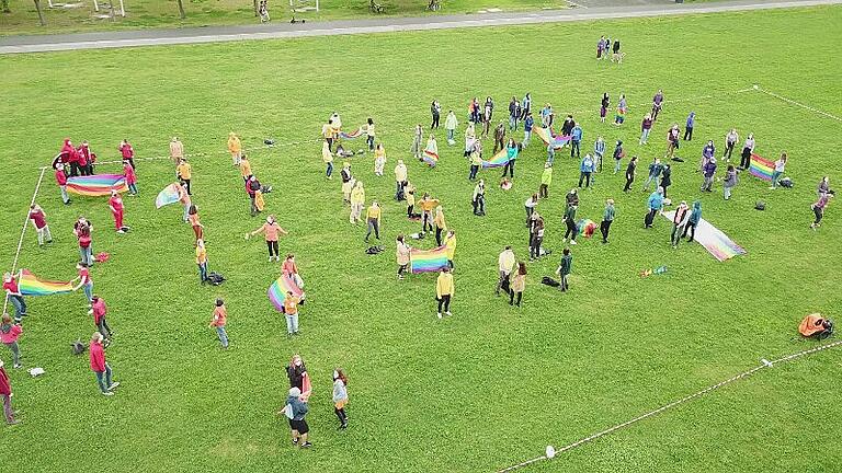 Rund 100&nbsp; bunt gekleidete Unterstützer und Unterstützerinnen bilden eine 'menschliche Regenbogenfahne'.