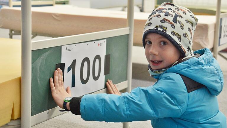 Der sechsjährige Emil Stäblein darf das Schild mit der Zahl 100 am letzten Bett in der Halle des Landkreises Rhön-Grabfeld anbringen.