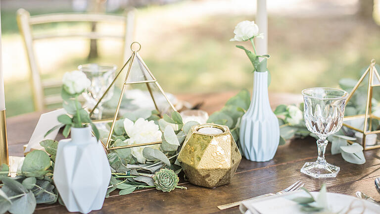 Table setting for an event party or wedding reception, decorated with geometric shape vases, gold candles eucalyptus branches and flowers.       -  Rustic or boho style wedding style arrangement