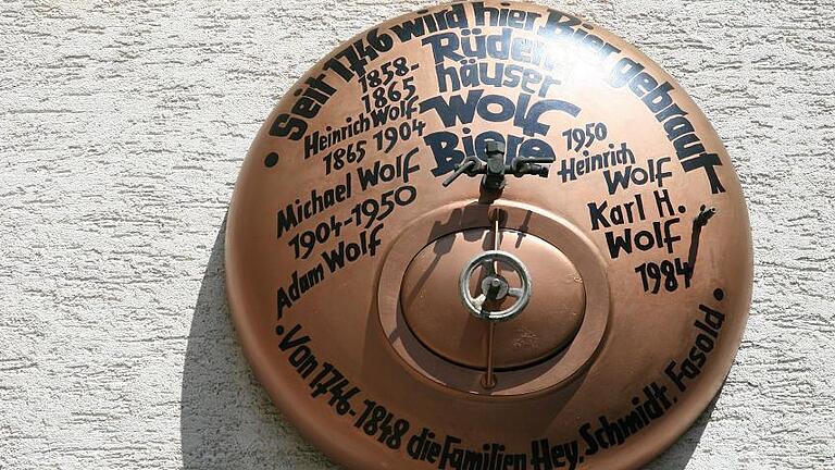 Historischer Hinweis: Ein Deckel vom Braukessel mit den Namen der Brauereibesitzer hängt an der Hauswand.