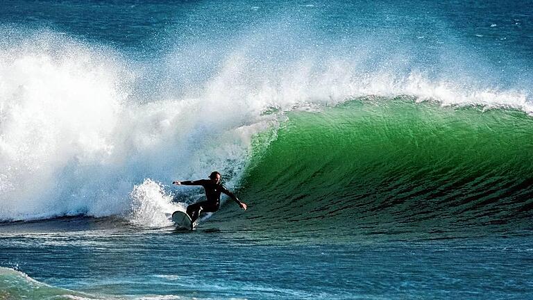 Beim Surfen vor dem Praia dos Supertubos: Das Surfbrett zieht eine helle Schneise ins Wasser, im Neoprenanzug mitten drin auf dem Longboard, von Gischt umrahmt Sebastian Emmert. Der Würzburger hat einen Ort gefunden, an dem man ganzjährig surfen kann &ndash; in Portugal.