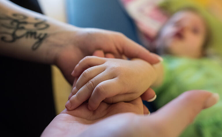 Ob Krankenhausbetreuung oder Intensivpflege-Einrichtung: Die Betreuung kranker Kinder ist teuer. Dieses Symbolbild zeigt eine Pflegefachkraft, die die Hand eines kleinen Mädchens hält.