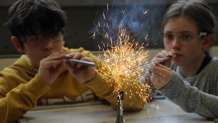 Orange-rot und weiß fliegen die Funken bei einem Experiment am Armin-Knab-Gymnasium, Kitzingen: Gregor und Lea pusten Eisenpulver und Magnesium in die Flamme des Bunsenbrenners.