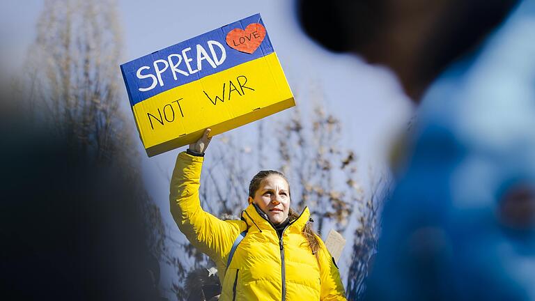 Symbolfoto: Eine Frau hält ein Plakat mit der Aufschrift 'Spread Love Not War' während einer Demonstration gegen den russischen Einmarsch in der Ukraine. Auch in Kitzingen findet am Dienstag, dem internationalen Frauentag, eine Mahnwache für den Frieden statt.