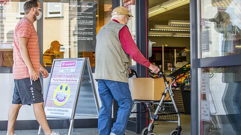 'Zutritt nur mit Mund-Nasen-Bedeckung' steht auf einem Aufsteller vor einem Supermarkt in Haßfurt. Doch haften die Geschäfte auch dafür, wenn ihre Kunden sich unvernünftig verhalten?