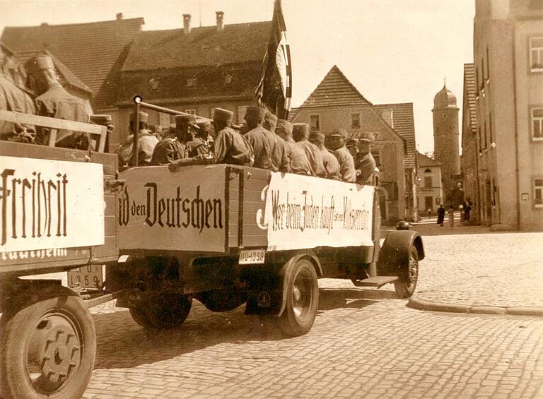 Spätestens nach Machtübernahme der Nationalsozialisten wurden die Restriktionen gegenüber den jüdischen Einwohnern der Stadt immer härter. Anhänger der Nazis trugen ihre judenfeindlichen Parolen offen zur Schau, wie auf diesem Bild. Es zeigt uniformierte SA-Männer auf Lastwagen, die über den Gerolzhöfer&nbsp; Marktplatz fahren. Auf dem Transparent auf der rechten Seitenwand des Lasters steht geschrieben: 'Wer beim Juden kauft ist ein Verräter'.