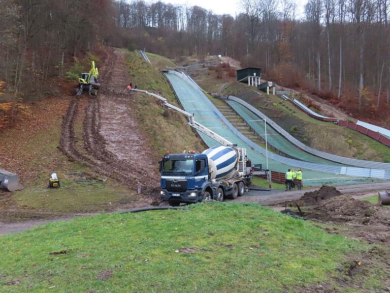 Als das weiter unten liegende Fundament betoniert wird, kommt der Beton mittels Betonpumpe vom Schanzenauslauf her. Links der Steigebagger, der sich mit langen krallenartigen Stützen regelrecht in den Hang beisst. Als das weiter unten liegende Fundament betoniert wird, kommt der Beton mittels Betonpumpe vom Schanzenauslauf her. Links der Steigebagger, der sich mit langen krallenartigen Stützen regelrecht in den Hang beisst.