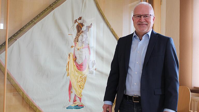 Manfred Schötz, Bürgermeister von Oberschwarzach, vor der Sebastiani-Fahne, die im Rathaus aufbewahrt wird. Die Fahne steht für ihn für die stolze Tradition der Marktgemeinde.