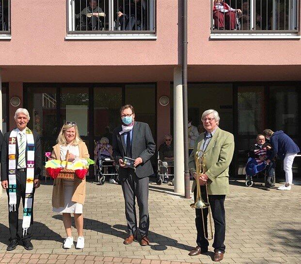 Pfarrer Bernd Töpfer, Gemeindeassistentin Ute Töpfer, Heimleiter Erik Schmekel, Posaunenchorleiter Bernd Richter vor dem Haus Lehmgruben bei der Übergabe eines Osterkorbes mit Briefen an die Senioren.