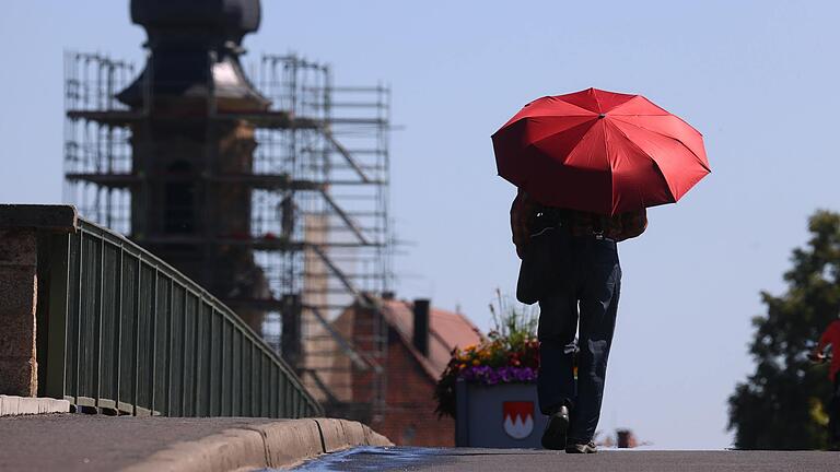 Ein Mann geht mit einem Schirm als Sonnenschutz über die Alte Mainbrücke in Kitzingen. Die Stadt hält seit 2015 den bayerischen Hitze-Rekord.&nbsp;