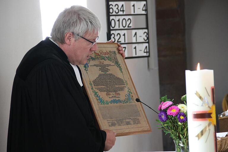 Pfarrer Reiner Apel zeigte während des Gottesdienstes ein überliefertes illustriertes Schmuckblatt der Urkunde, die im Grundstein der Kirche ruht.