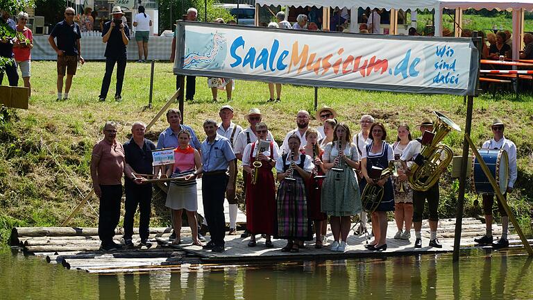 Floßübergabe auf dem großen Holzfloß auf der Saale mit von links: Kuno Holzheimer (Leiter der Musikakademie Hammelburg), Landrat Thomas Bold (Bad Kissingen), Gräfendorfs Bürgermeister Johannes Wagenpfahl, Landrätin Sabine Sitter (Main-Spessart), Thomas Schiebel vom Bezirk Unterfranken und der Musikkapelle Michelau. Floßübergabe auf dem großen Holzfloß auf der Saale mit von links: Kuno Holzheimer (Leiter der Musikakademie Hammelburg), Landrat Thomas Bold (Bad Kissingen), Gräfendorfs Bürgermeister Johannes Wagenpfahl, Landrätin Sabine Sitter (Main-Spessart), Thomas Schiebel vom Bezirk Unterfranken und der Musikkapelle Michelau.