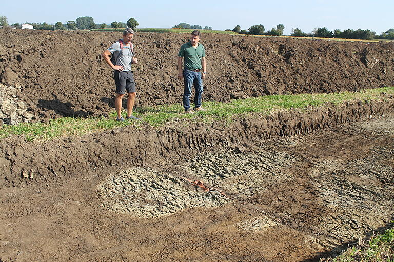 Als in den Sondierungsstreifen mit dem Bagger der Humus abgezogen wurde, kamen im September 2021 auf dem Norma-Baugrundstück zahlreiche Verfärbungen im anstehenden Erdreich zum Vorschein. Der Gerolzhöfer Museumsleiter Bertram Schulz (links) und Architekt Martin Giedl begutachten hier eine Stelle mit natürlichen, geologisch bedingten Verfärbungen. Angeschnitten wurde auch eine Drainage-Leitung mit roten Tonrohren.