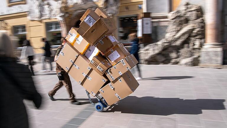 Symbolbild: Ein Paketzulieferer transportiert mit einer Sackkarre mehrere Pakete durch eine Fußgängerzone.