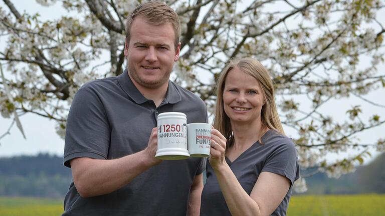 Beim großen Fest Ende Mai sind auch Jubiläumsartikel zu haben. Florian Erhard und Bettina Bonengel zeigen zum Beispiel einen Bierkrug und eine Tasse.