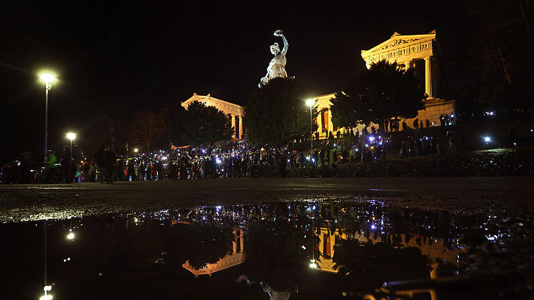 Demonstrationen gegen rechts - München.jpeg       -  Menschen unter der Münchner Ruhmeshalle und der Bavaria spiegeln sich auf der Theresienwiese in einer Regenpfütze bei einer Demonstration  gegen Rassismus, Antisemitismus und Hetze.