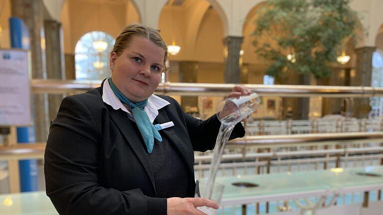 Brunnenfrau Lisa Lausenmeyer schwenkt das Heilwasser von Glas zu Glas. Der Heilwasserausschank in der Brunnenhalle ist wieder geöffnet. Foto: Anja Vorndran       -  Brunnenfrau Lisa Lausenmeyer schwenkt das Heilwasser von Glas zu Glas. Der Heilwasserausschank in der Brunnenhalle ist wieder geöffnet. Foto: Anja Vorndran