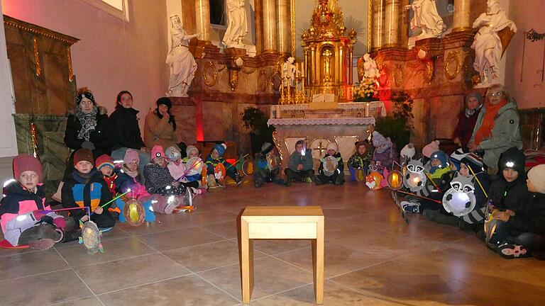 Die Vorschulkinder des Kindergartens St. Sebastian im Chorraum der Unterspiesheimer Kirche mit ihren Martinslaternen. Im Hintergrund die Kolleginnen des Erzieherinnenteams, die die Martinslieder mit ihnen geübt haben und das Martinsspiel vorbereitet haben.