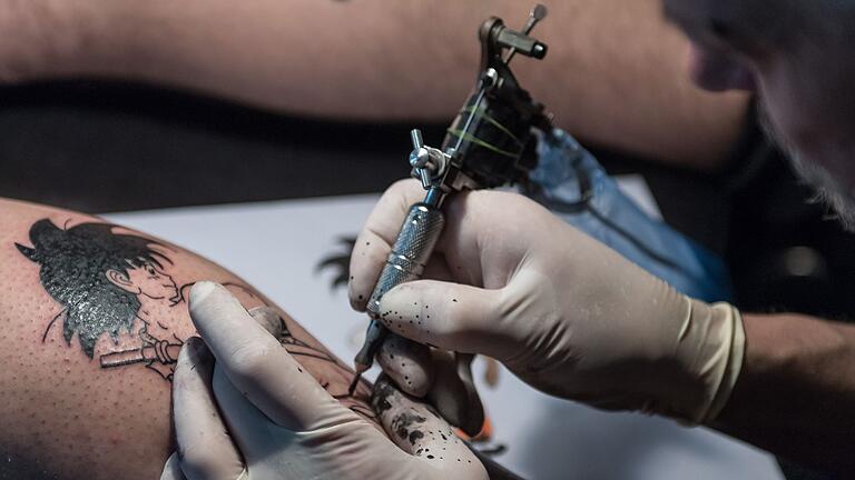 Tätowierer arbeitet an einem Tattoo - In ein frisch gestochenes Tattoo auf keinen Fall Keime geraten, die für Infektionen sorgen können. Tätowierer arbeitet an einem Tattoo - In ein frisch gestochenes Tattoo auf keinen Fall Keime geraten, die für Infektionen sorgen können.