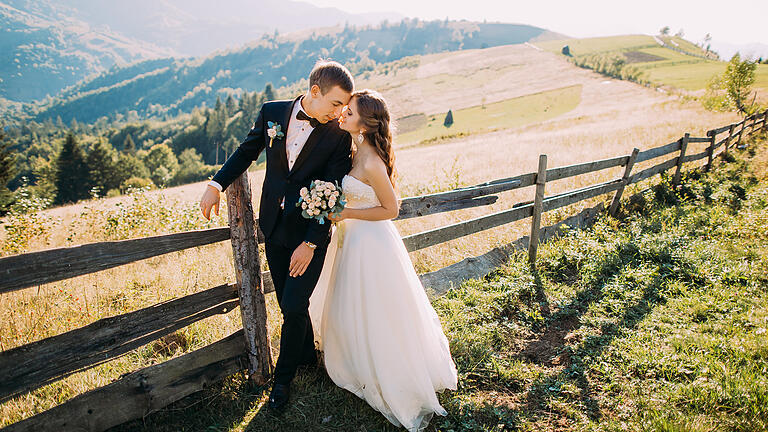 Bride and groom standing embracing near wooden fence on the       -  Eine Hochzeit auf dem Land verspricht unvergessene Moment vor atemberaubenden Naturpanorama. Trotzdem gibt es einiges zu beachten.