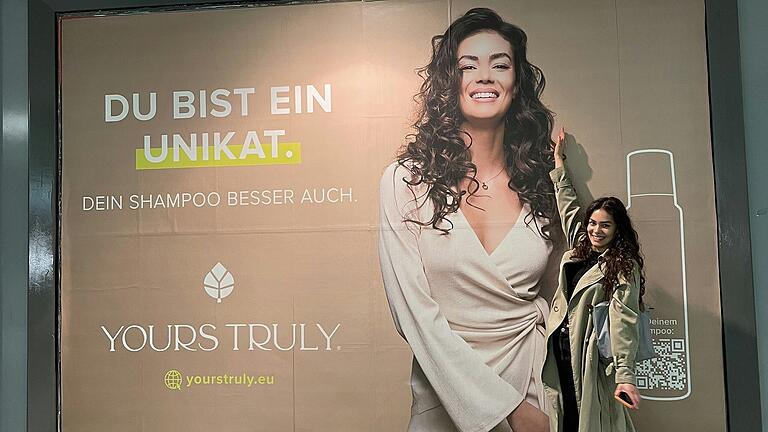 Caroline Schmidt steht hier vor einem Plakat am Frankfurter Hauptbahnhof mit ihrem Konterfei.