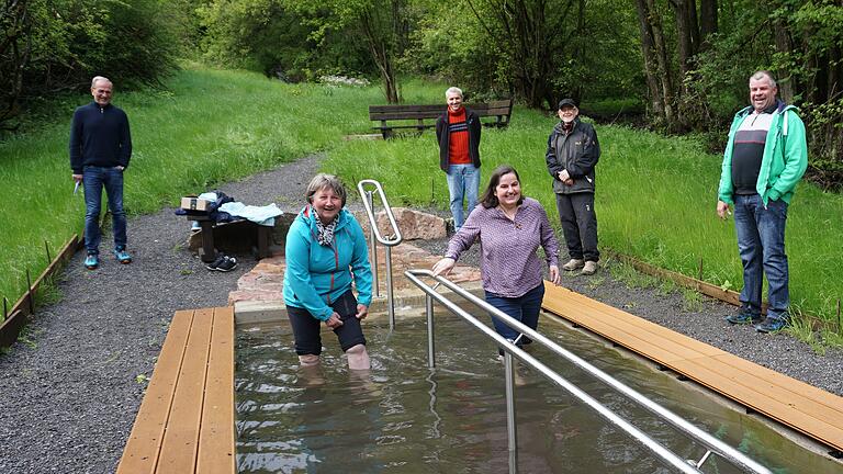 „Gesundheitskneippanlage am Kreuzberg“ – die idyllisch gelegene Kneippanlage oberhalb von Sandberg ist in Betrieb. Bürgermeisterin Sonja Reubelt (rechts im Wasser) und Ute Holzheimer (links) ließen es sich nicht nehmen, zum Auftakt ins kühle Nass zu steigen. Mit im Bild von links hinten:  Thomas Zehe (Wanderwart des Rhönklubs Walddörfer), Thorsten Kirchen (Freizeit- und Tourimusnetzwerk), Pius Bühner (Kassier des Rhönklubs Walddörfer) und Marco Voll.