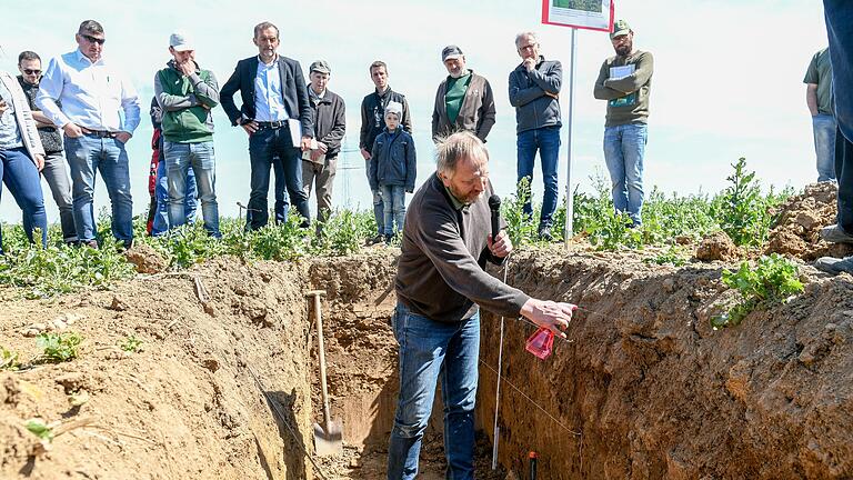 Am Bodenprofil zeigt Joachim Liebler von der Regierung von Unterfranken, wie sich die bodenschonende Arbeitsweise auf das Bodenleben auswirkt.