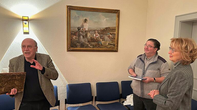Friedrich Tasch mit alter Chronik, Bürgermeister Karl Dieter Fuchs und Spenderin Rajka Leibach vor dem von ihr überreichten Gemälde aus den Mainstockheimer Weinbergen.