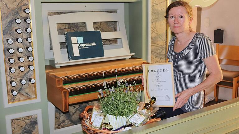 Gudrun Vollmuth an der Orgel in Abtswind mit Urkunde und Geschenkkorb.