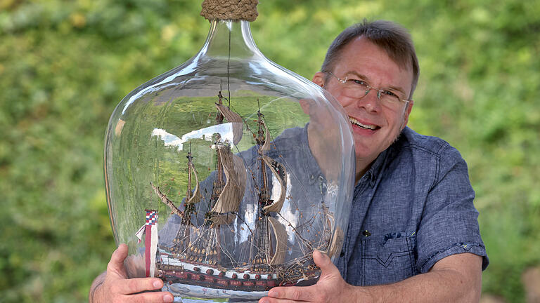 Buddelschiffbauer will neuen Rekord aufstellen       -  Matthias Schultz sitzt neben einem von ihm gebauten 40 Zentimeter hohen und 38 Zentimeter langem Buddelschiff welches in einem 50 Liter fassenden Gärballon hängt. Mit dem «größten freischwebenden Buddelschiff der Welt» will der Modellbauer in das Guinness-Buch der Rekorde kommen.