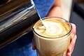 Eine Person gießt aufgeschäumte Milch in ein Glas       -  Ist der Latte macchiato mit Hafermilch ein Problem für den Blutzuckerspiegel, wie es im Netz oft heißt? So pauschal kann man das nicht sagen.