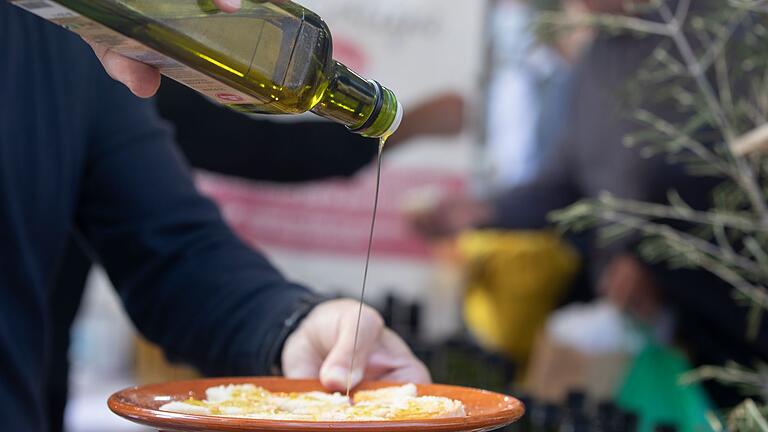 Ein Mann träufelt Olivenöl auf ein Stück Brot       -  Die Stiftung Warentest fand große Unterschiede in Preis und Qualität bei Olivenöl.