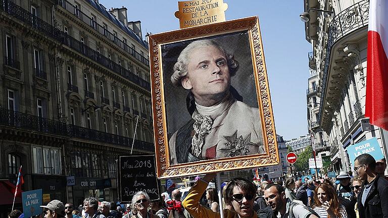 Proteste zum 1. Jahrestag der Amtseinführung von Macron       -  Vor dem ersten Jahrestag der Amtseinführung von Präsident Emmanuel Macron kommt es in Paris zu Protesten Zehntausender Menschen. Demonstranten haben am Samstag ein Gemälde dabei, das den Präsidenten als König Ludwig XVI. zeigt.