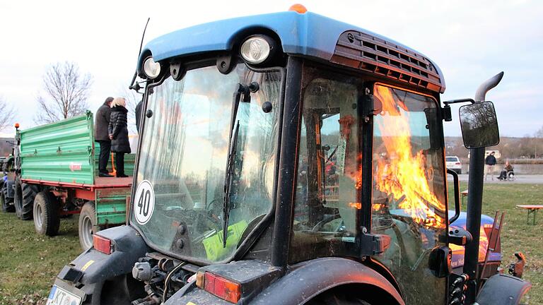 In den Fenstern eines Kleintraktors spiegelt sich das entzündete Mahnfeuer unterhalb der Astheimer Mainbrücke. Auf einem Wagen sprechen Vertreter der Initiative 'Land schafft Verbindung' und Politiker zu den Teilnehmern der Protestaktion.