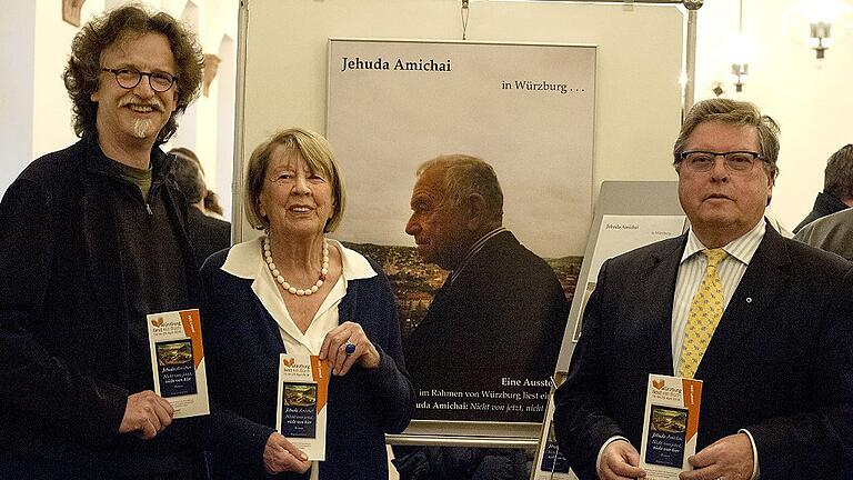 Daniel Osthoff, Rosa Grimm und Bürgermeister Adolf Bauer vor dem Plakat der Amichai-Ausstellung im Rathaus. Das Plakat zeigt den Schriftsteller, der von der Festung aus auf Würzburg blickt.