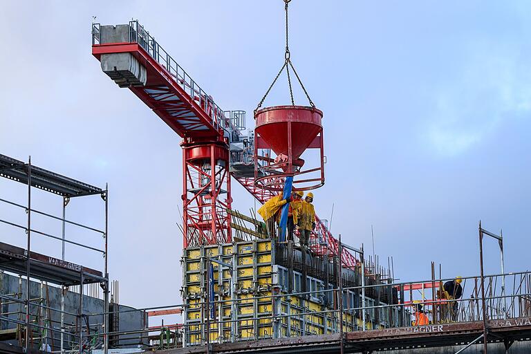 Hoch oben gießen Bauarbeiter Beton in eine Verschalung. Mehrere Stockwerke des Gebäudes fehlen noch.