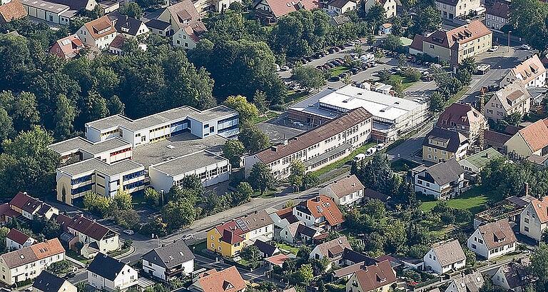 Einen guten Überblick über die Situation auf dem Schulgelände am Lülsfelder Weg mit dem östlich angrenzenden Großparkplatz vermittelt diese Luftaufnahme aus dem Jahr 2009. Zu sehen sind auf dem Bild die wagenburgartig angelegten Betonklötze der Mittelschule mit der integrierten kleinen Turnhalle im Vordergrund ebenso wie das vorgelagerte Grundschulgebäude von 1954 mit der zum Zeitpunkt der Aufnahme gerade östlich angebauten Zweifachhalle.