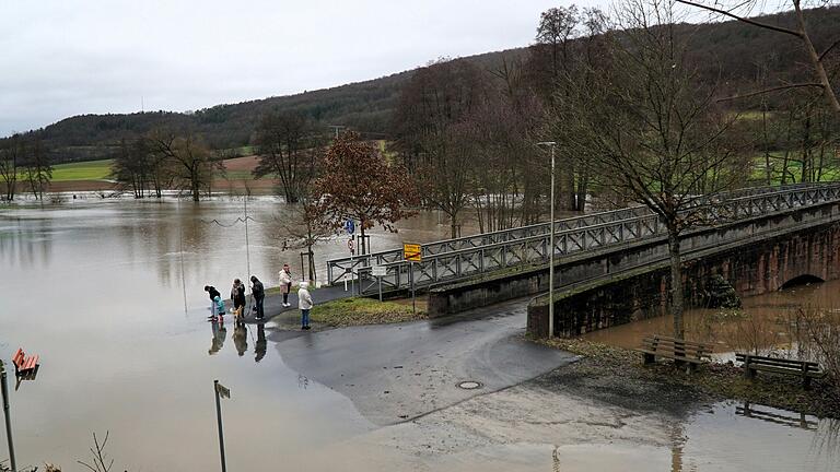 Anwohner begutachten das Hochwasser in Wolfsmünster an der Fußgängerbrücke und der Autobrücke rechts daneben. Anwohner begutachten das Hochwasser in Wolfsmünster an der Fußgängerbrücke und der Autobrücke rechts daneben.