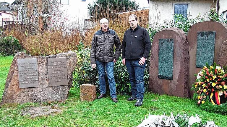 Zentrale Gedenkstelle in Burgsinn: Bürgermeister Robert Herold (rechts) und Initiator Klaus Hofmann inmitten der Gedenkstelle mit dem Kriegerdenkmal auf der rechten und den neuen Gedenktafeln auf der linken Seite.