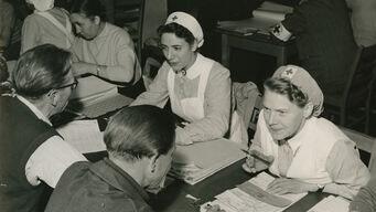 Rotkreuz-Helferinnen mit Kriegsheimkehrer aus der Sowjetunion in einem Büro des DRK-Suchdienstes im Lager Friedland (Oktober 1955).