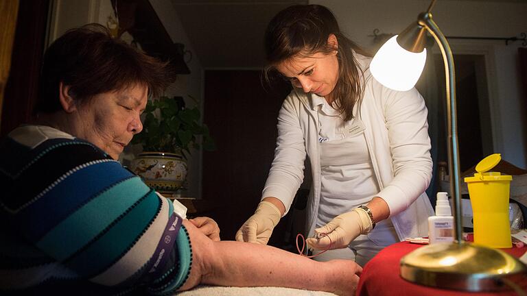 Eine Versorgungsassistentin in der Hausarztpraxis, genannt Verah, nimmt einer Patientin bei einem Hausbesuch Blut ab.