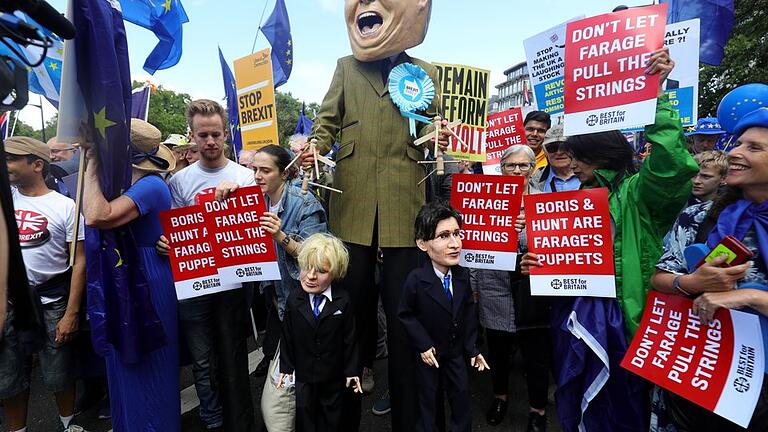 Puppenspieler       -  Ein Demonstrant (M) hat sich für den Protestzug als Nigel Farage, Vorsitzender der Brexit-Partei, verkleidet - und hält die Schnüre der Marionetten &bdquo;Boris Johnson&rdquo; und &bdquo;Jeremy Hunt&rdquo; in den Händen.