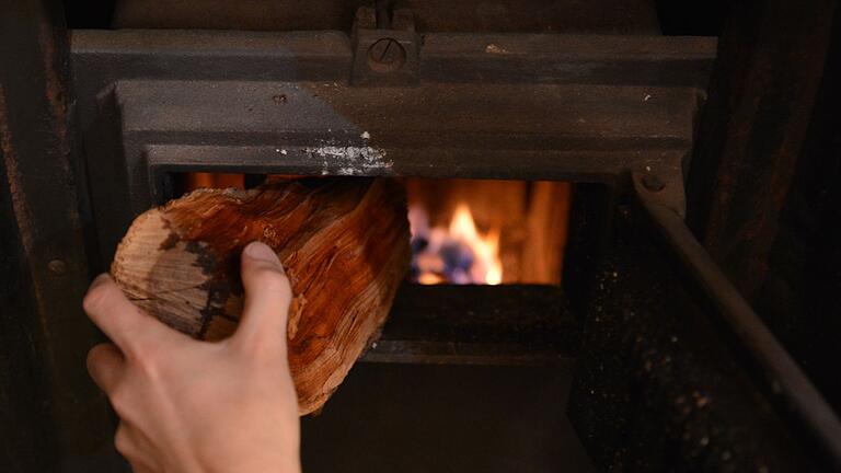 Holzfeuer im Kachelofen       -  Ein Mann legt ein Stück Holz in einem Kachelofen nach.