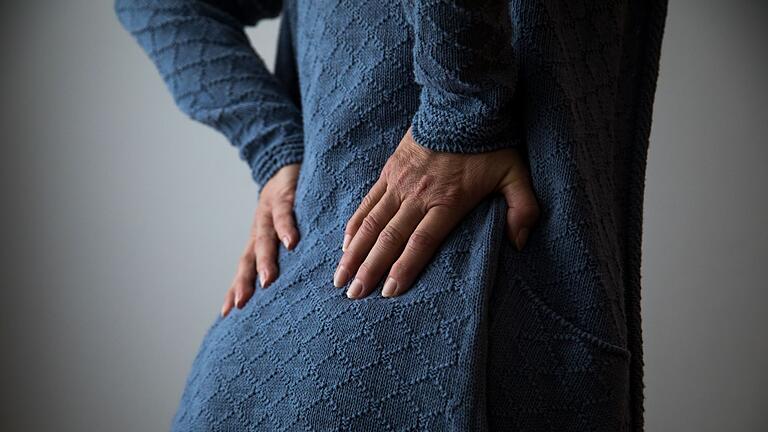 Frau hält sich den unteren Rücken - Schmerzen während der Periode können in den unteren Rücken ausstrahlen. Frau hält sich den unteren Rücken - Schmerzen während der Periode können in den unteren Rücken ausstrahlen.