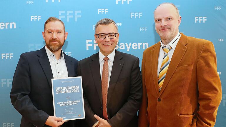 Johannes Bröstler (links) und Oliver Hauguth (rechts) vom Movie im Luitpoldhaus bekommt die Urkunde für den Filmprogrammpreis von Staatsminister Florian Hermann überreicht.