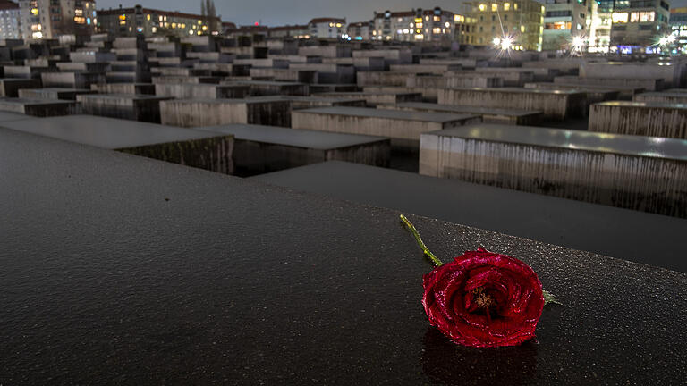 ARCHIV - 28.01.2019, Berlin: Eine Rose, bedeckt von Regentropfen, liegt in der Dunkelheit auf einer der nassen Betonstelen des Denkmals für die ermordeten Juden Europas. (zu dpa «Grütters: Relativierung von NS-Verbrechen entschieden begegnen») Foto: Stefan Jaitner/dpa +++ dpa-Bildfunk +++