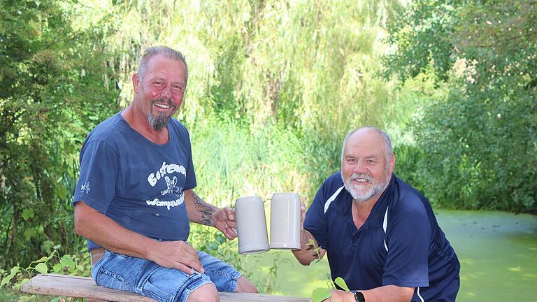 Ein Prosit auf den runden Geburtstag der Bostemer Wampewockler: Präsident Roland Happel (links) und Ehrenpräsident Paul Zimmer stoßen im Wampewockler-Biotop, der ehemaligen Bastheimer Kläranlage, miteinander an.&nbsp;